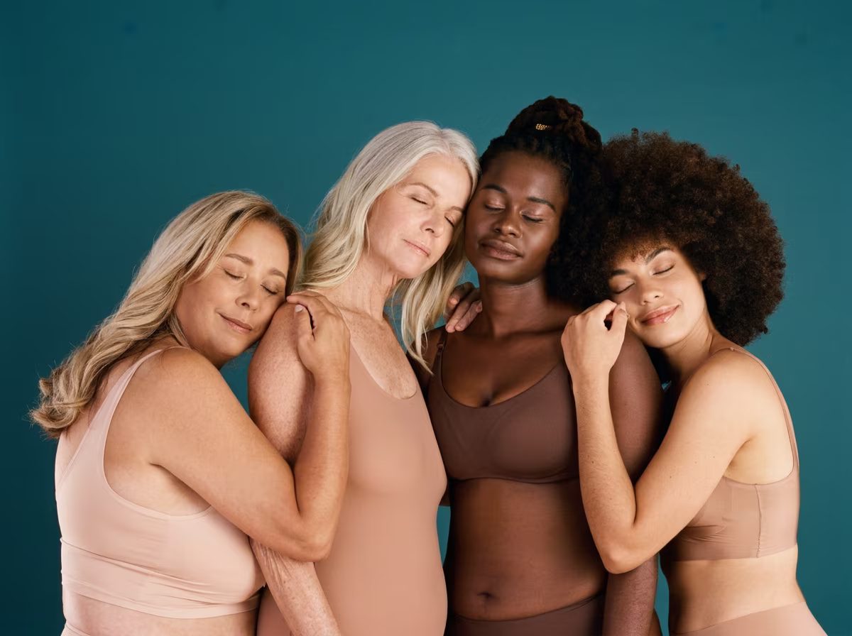 Quatre femmes d'âges et d'origines variés en sous-vêtements, serrées les unes contre les autres, les yeux fermés et apaisées, sur fond bleu canard