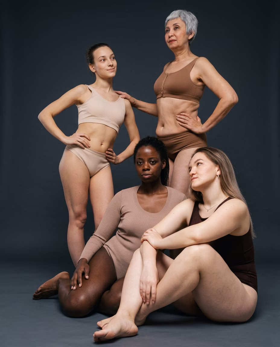 Quatre femmes d'âges et de morphologies variés en sous-vêtements aux tons nude, posant ensemble sur fond gris foncé