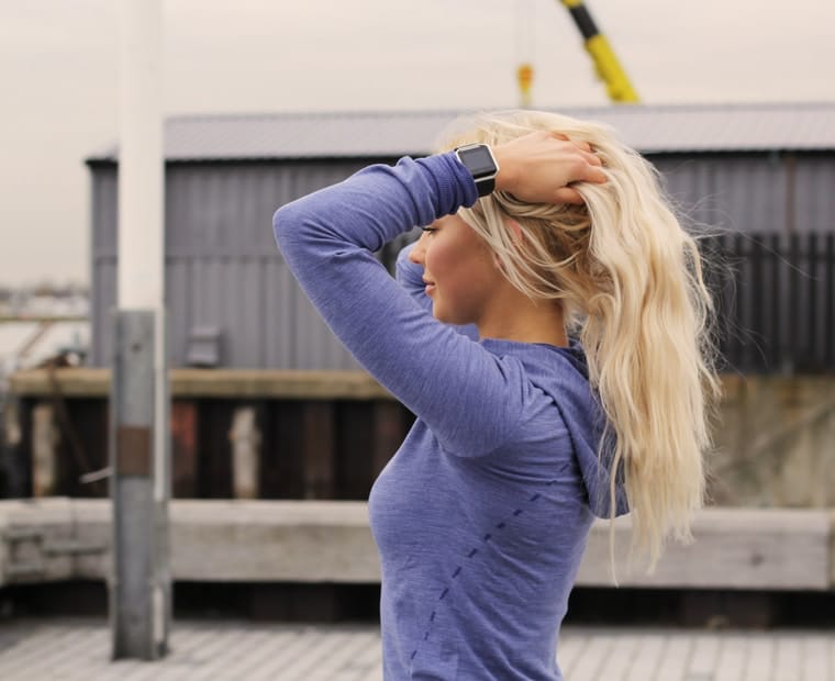 Femme blonde en haut bleu attachant ses cheveux en plein air, avant une séance de sport