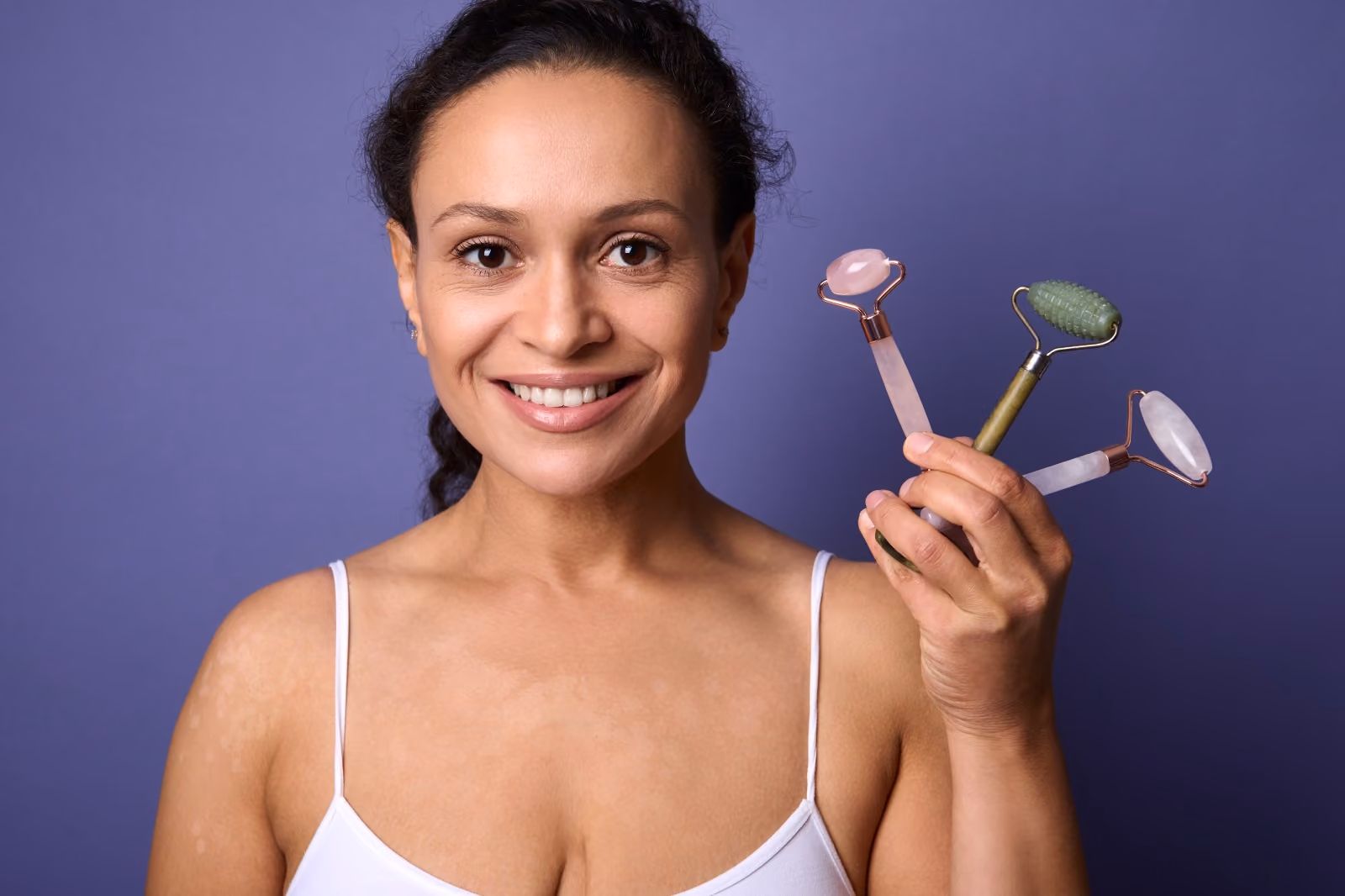 Femme souriante tenant des rouleaux de massage pour le visage près de ses joues