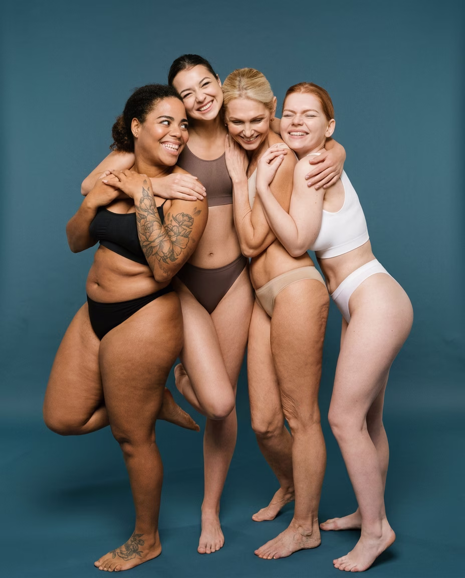 Groupe de femmes rieuses aux morphologies variées, en sous-vêtements, serrées les unes contre les autres sur fond bleu pétrole